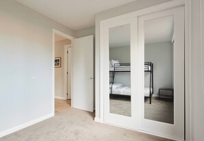 Une chambre avec un lit superposé, une porte avec un miroir et un couloir menant à une autre pièce.