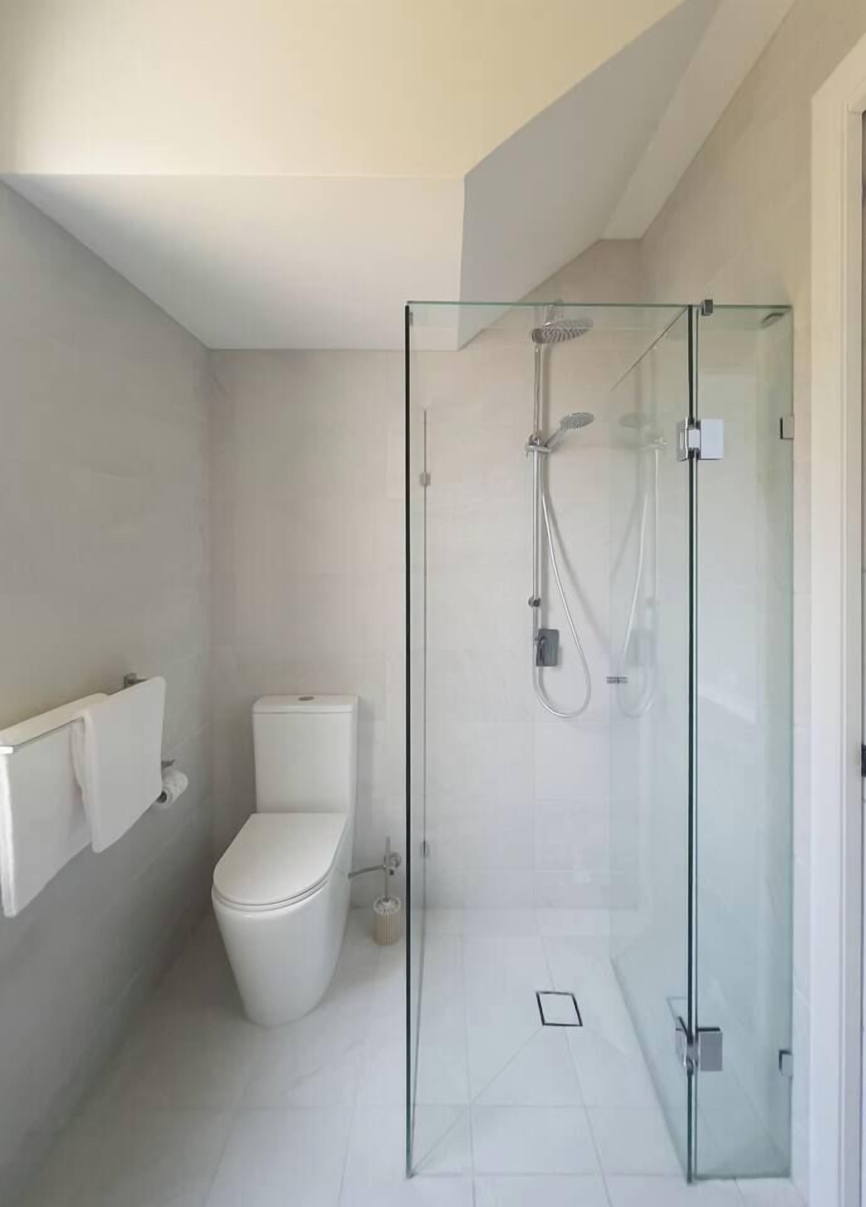 A modern bathroom with a glass-enclosed shower, a toilet, and a towel rack.