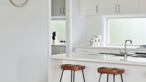 Eine moderne Küche mit weißen Schränken, einer zentralen Kochinsel mit Barhocker und einer dekorativen Wandgestaltung.