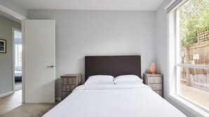 Ein Schlafzimmer mit einem großen Bett, einem hölzernen Kopfteil, zwei Nachttischen und einem Fenster mit Blick auf Grünfläche.
