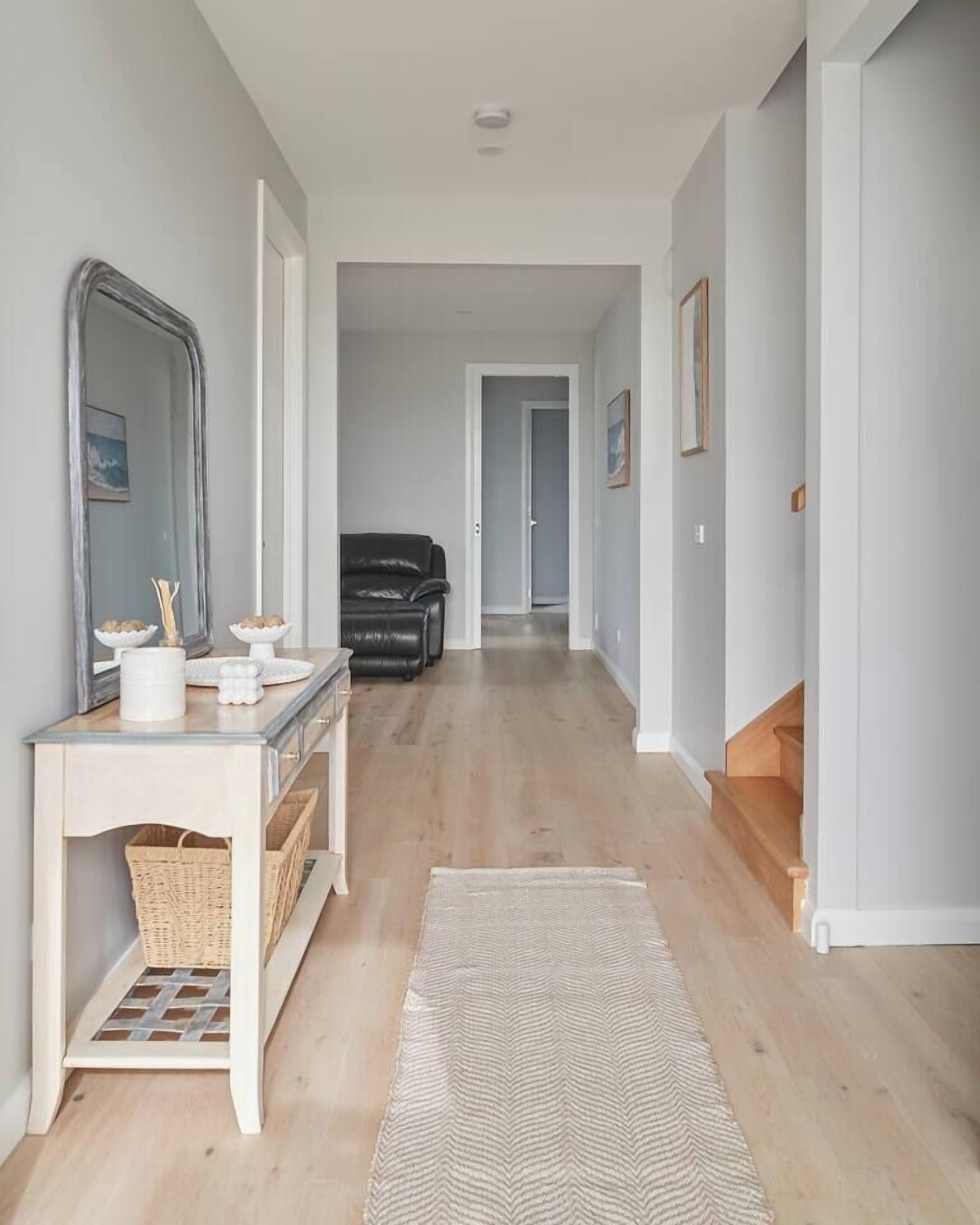 Un couloir avec une console blanche, un miroir, un fauteuil en cuir noir et un escalier en bois.