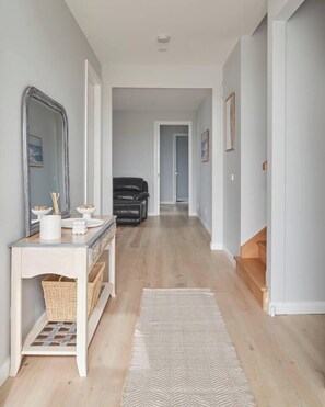 A hallway with a white console table, a mirror, a black leather chair, and a wooden staircase. - Harbour Horizons Balcony BBQs and Calm Water Views (Clifton Springs)