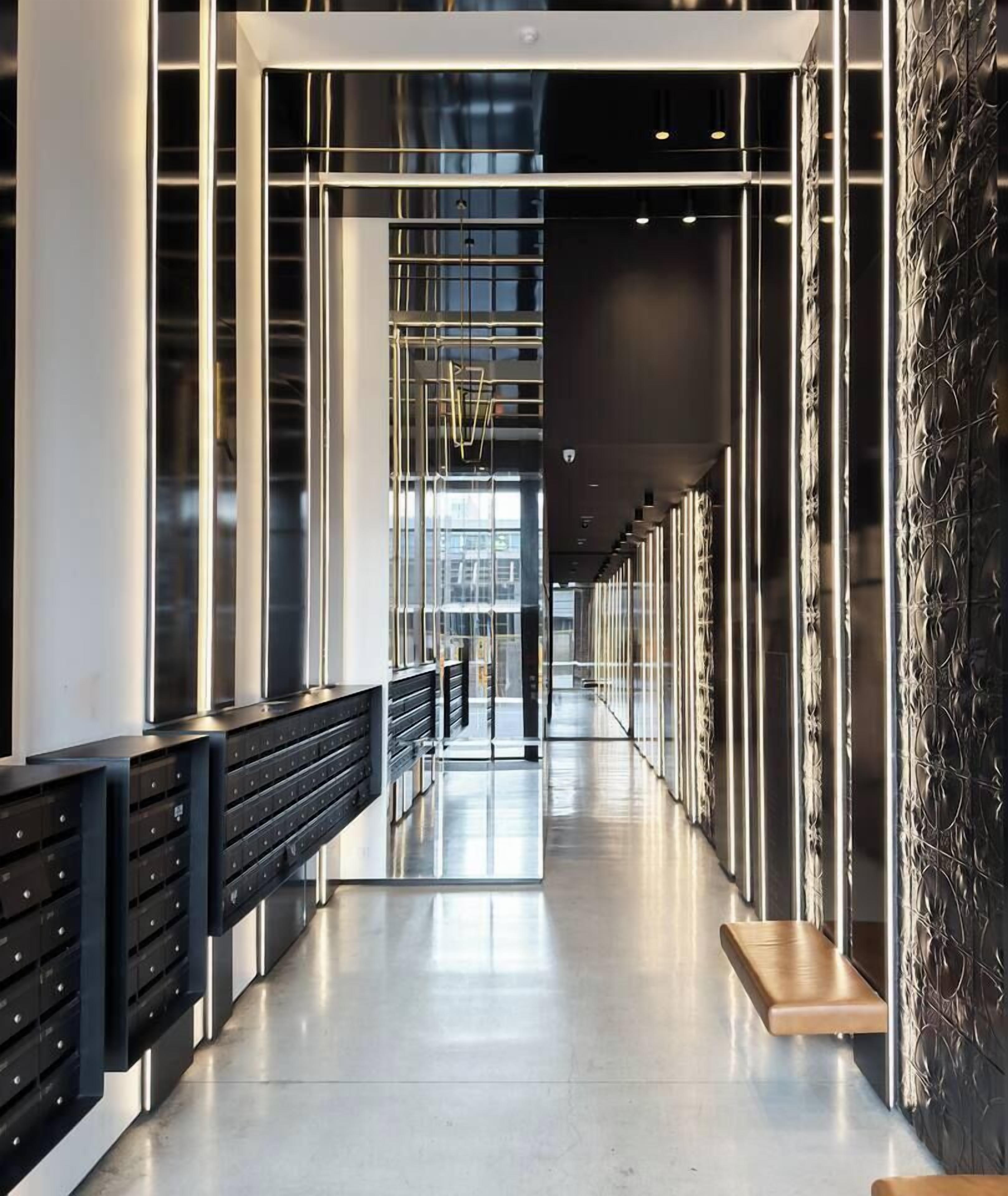 A modern hallway with a reflective floor, a black railing, and a patterned wall on the right.