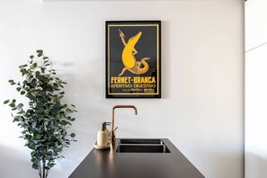 A framed poster on a wall, a potted plant, and a modern sink with a faucet. - Fitzroyals Uchi in Melbournes Multicultural Hub (Fitzroy)