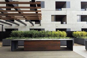 A modern outdoor seating area with a wooden bench and planters. - Fitzroyals Uchi in Melbournes Multicultural Hub (Fitzroy)