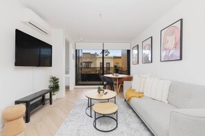 A modern living room with a sofa, coffee table, and a TV mounted on the wall. - Fitzroyals Uchi in Melbournes Multicultural Hub (Fitzroy)