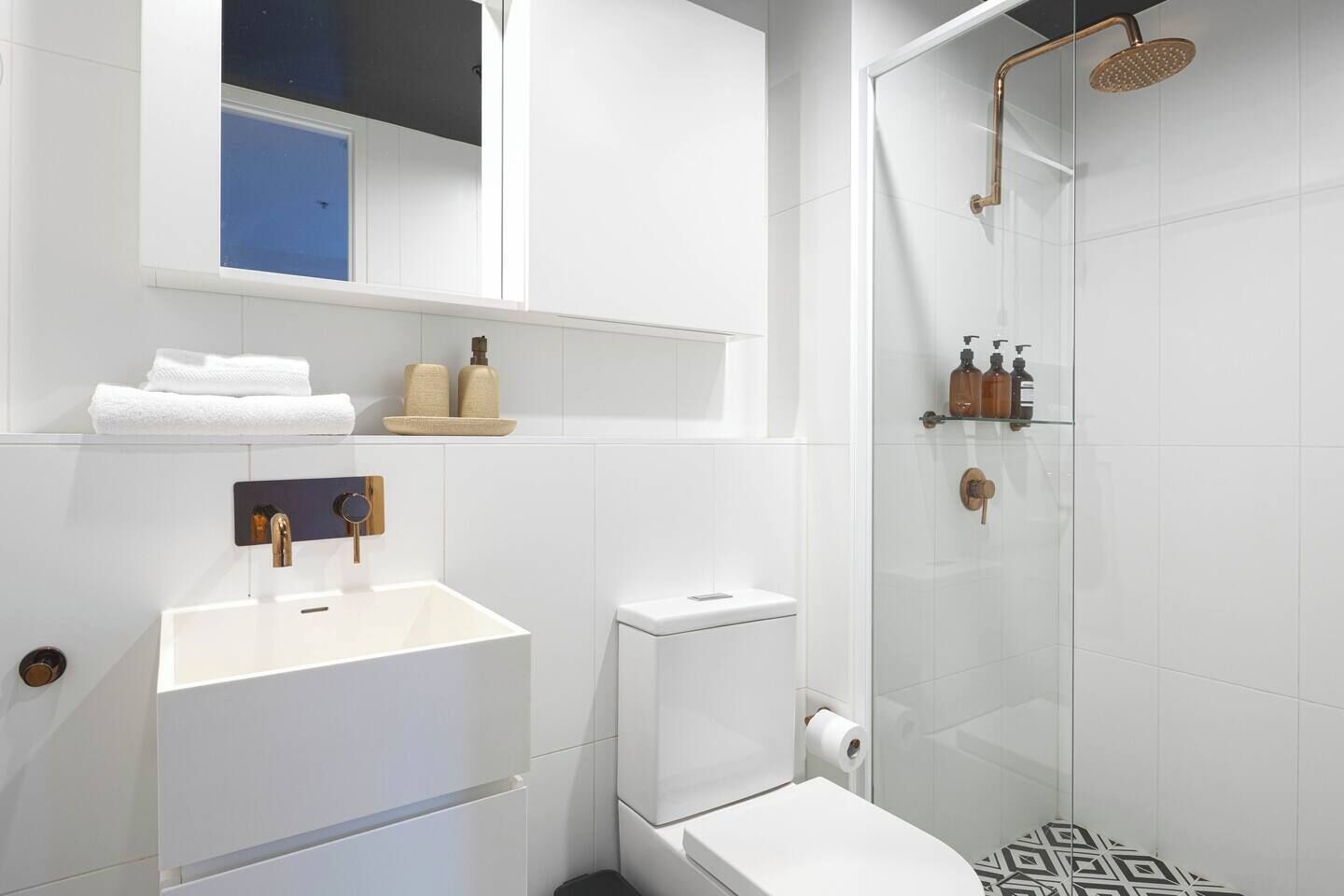 A modern bathroom with a white sink, toilet, and glass-enclosed shower.