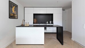 Uma cozinha moderna com armários brancos, bancada preta e piso de madeira em padrão herringbone.