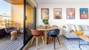 Uma sala de estar moderna com uma mesa redonda de madeira, duas cadeiras, um sofá e uma varanda com cadeiras de vime.