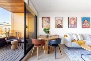 A modern living room with a round wooden table, two chairs, a sofa, and a balcony with wicker chairs. - Fitzroyals Uchi in Melbournes Multicultural Hub (Fitzroy)