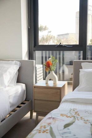 Una habitació d'hotel moderna amb un llit, una taula de nit amb un ram de flors i vista a la ciutat a través de grans finestres.
