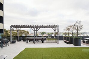 An outdoor patio area with a pergola, seating, planters, and a view of the cityscape. - Urban Drift Cosy Balcony Nook near Waterfront (Geelong)