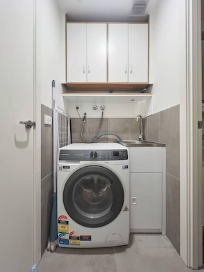 A compact laundry room with a front-loading washing machine, a sink, and a cabinet above. - Urban Drift Cosy Balcony Nook near Waterfront (Geelong)