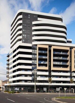 Un edifici de diverses plantes amb façana corbada, grans finestres i zona comercial a la planta baixa amb cartelleria.