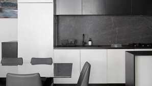 A modern kitchen with a dining area, featuring a minimalist design with white and dark grey cabinetry, a black countertop, and a dining table with chairs. - Modern Minimalism Slate Chic in the City (North Melbourne)