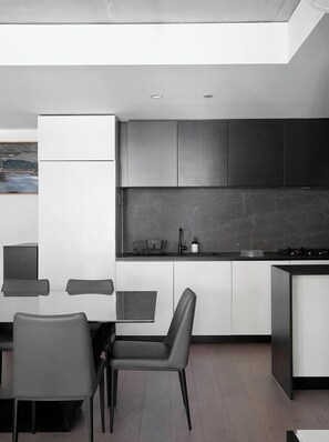 Eine moderne Küche mit Essbereich, die ein minimalistisches Design mit weißen und dunkelgrauen Schränken sowie einer schwarzen Arbeitsplatte und einem Esstisch mit Stühlen zeigt.