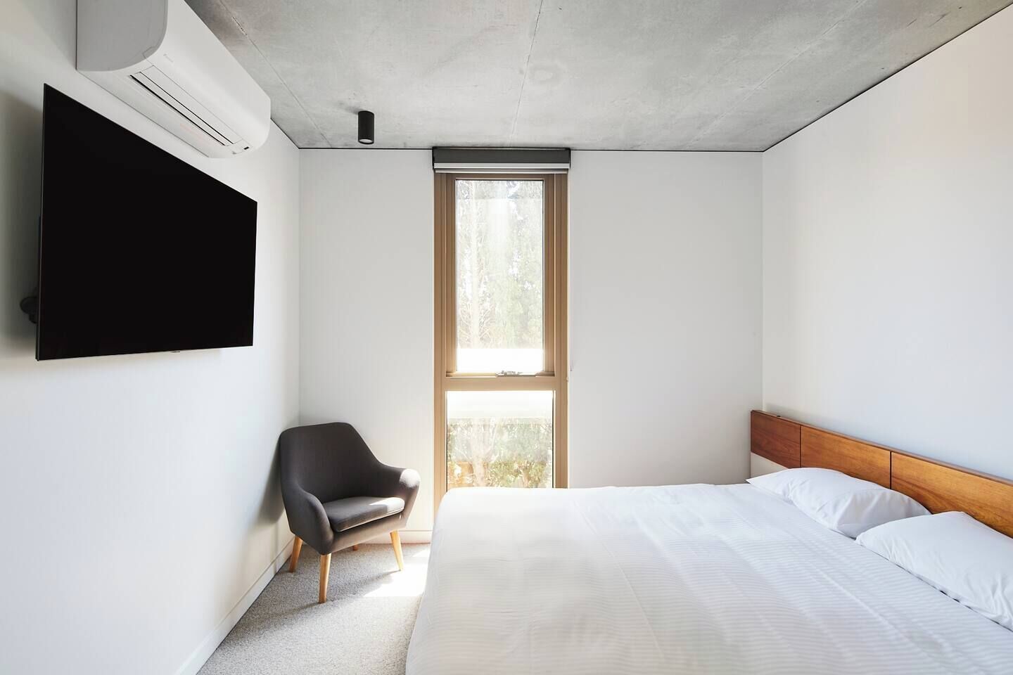 A bedroom with a bed, a chair, a TV, and a window.
