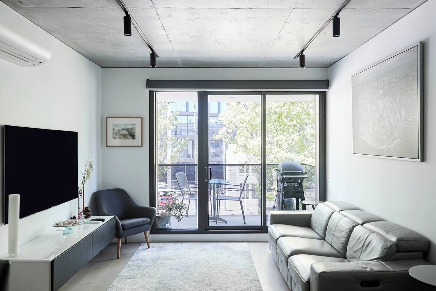 A modern living room with a sofa, a chair, a TV, and a balcony with a grill.
