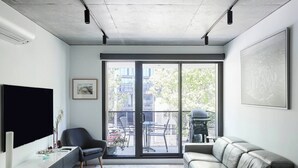 A modern living room with a sofa, a chair, a TV, and a balcony with a grill. - Modern Minimalism Slate Chic in the City (North Melbourne)