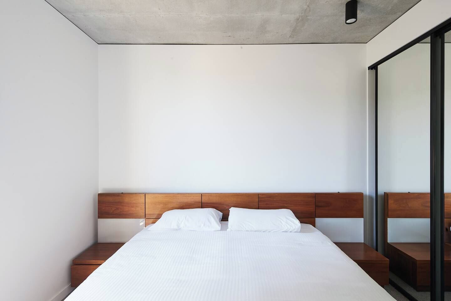 Un dormitorio minimalista con cabecera de madera, una cama grande con ropa de cama blanca y un panel de vidrio en un lateral.