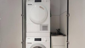 A compact laundry room with stacked washing machines and a small cabinet. - Modern Minimalism Slate Chic in the City (North Melbourne)