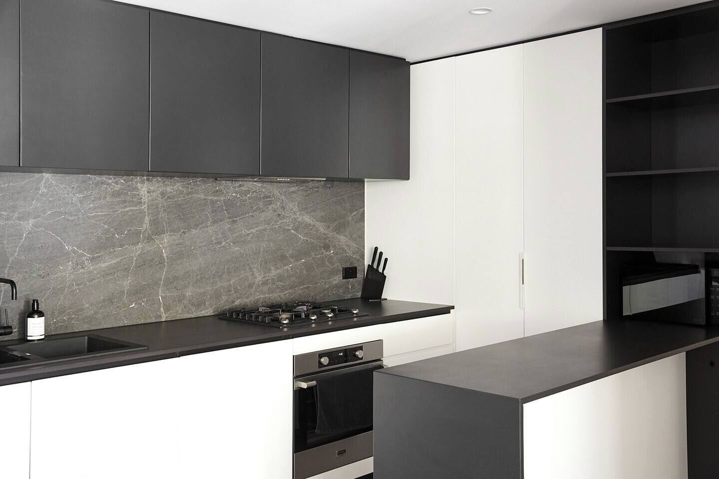 Une cuisine moderne avec des meubles de couleur sombre, un pare-feu en marbre et un four encastré.