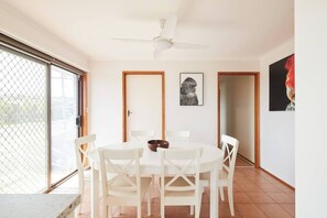 Ein Essbereich mit einem runden Tisch und weißen Stühlen, einem Deckenventilator und einer zur Außenwelt führenden Tür.