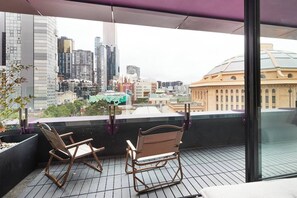 Un balcon avec deux fauteuils à bascule, une rambarde en verre et une vue sur la ville.