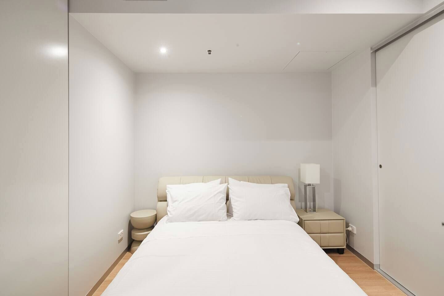 Ein schlicht eingerichtetes Hotelzimmer mit einem großen Bett, einem Nachttisch mit Lampe und einem Kleiderschrank.