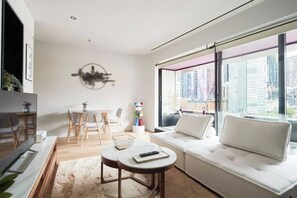 A modern living room with a sofa, a dining table, and chairs. There is a large window with a view of buildings. - Urban Artistry Loft A Haven Above the Bustle (Melbourne)