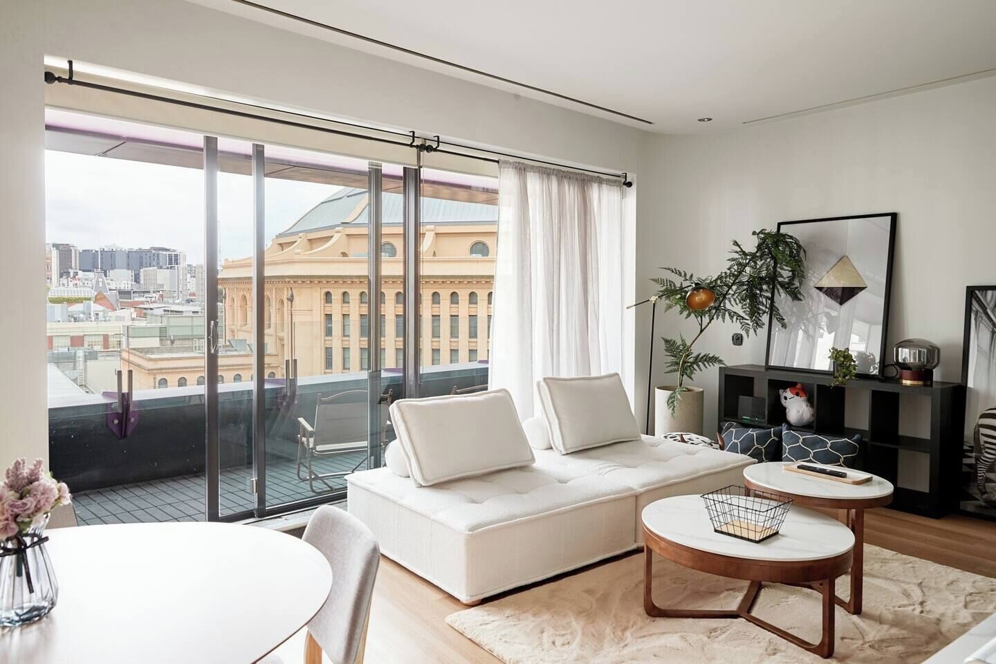 En moderne stue med en sofa, et sofabord og udsigt til et bybillede gennem store vinduer.
