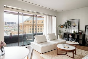 A modern living room with a sofa, a coffee table, and a view of a cityscape through large windows. - Urban Artistry Loft A Haven Above the Bustle (Melbourne)