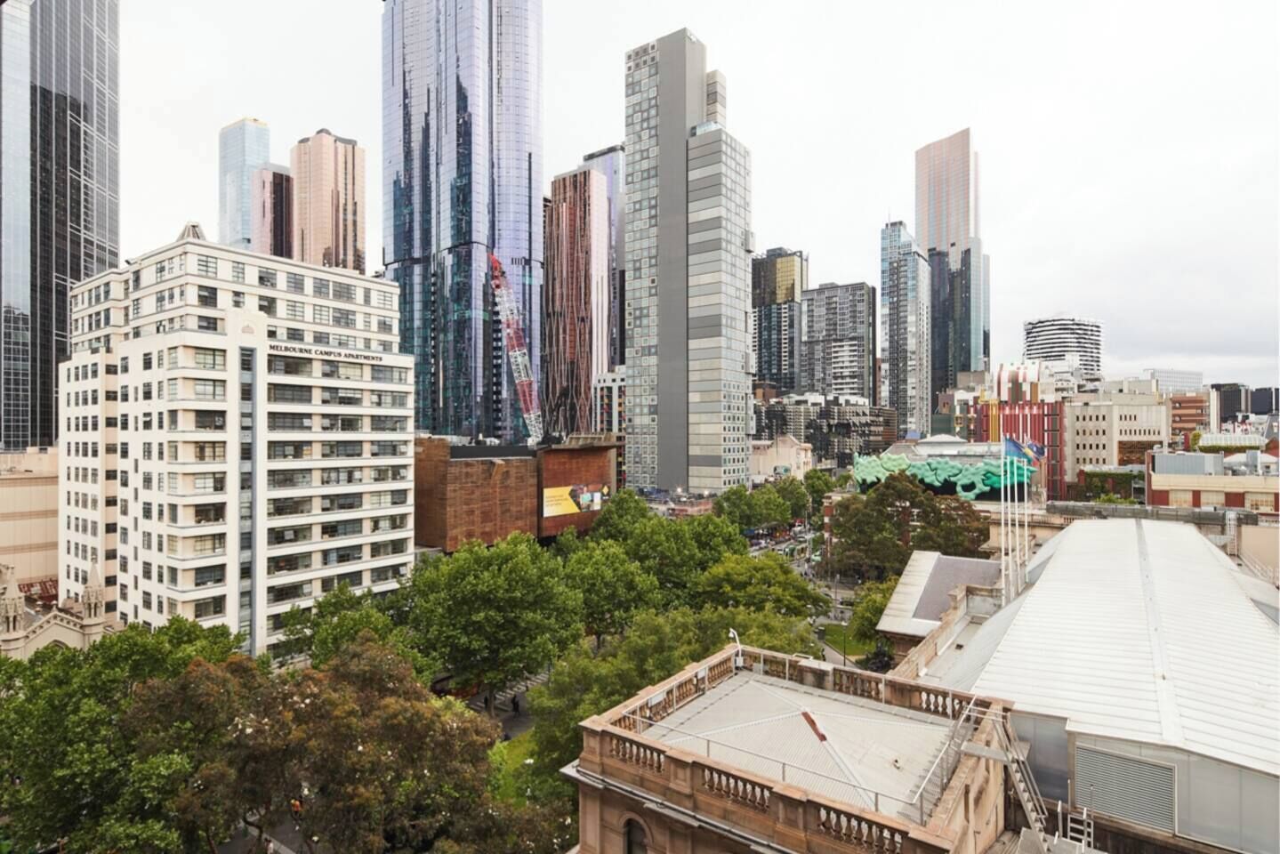 A cityscape with high-rise buildings, including a prominent white building with multiple floors and a large green structure in the background.