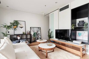 Un salon moderne avec un canapé blanc, une table basse, un téléviseur et une bibliothèque.