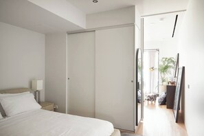 A bedroom with a bed, a nightstand, a lamp, a wardrobe, and a mirror. - Urban Artistry Loft A Haven Above the Bustle (Melbourne)