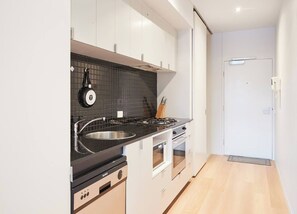 A modern kitchen with a black countertop, stainless steel sink, and white cabinets. - Urban Artistry Loft A Haven Above the Bustle (Melbourne)