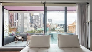 A modern hotel room with a large balcony, a bed with two pillows, a chair, and a view of a cityscape. - Urban Artistry Loft A Haven Above the Bustle (Melbourne)