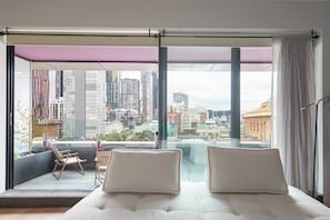 A modern hotel room with a large balcony, a bed with two pillows, a chair, and a view of a cityscape. - Urban Artistry Loft A Haven Above the Bustle (Melbourne)