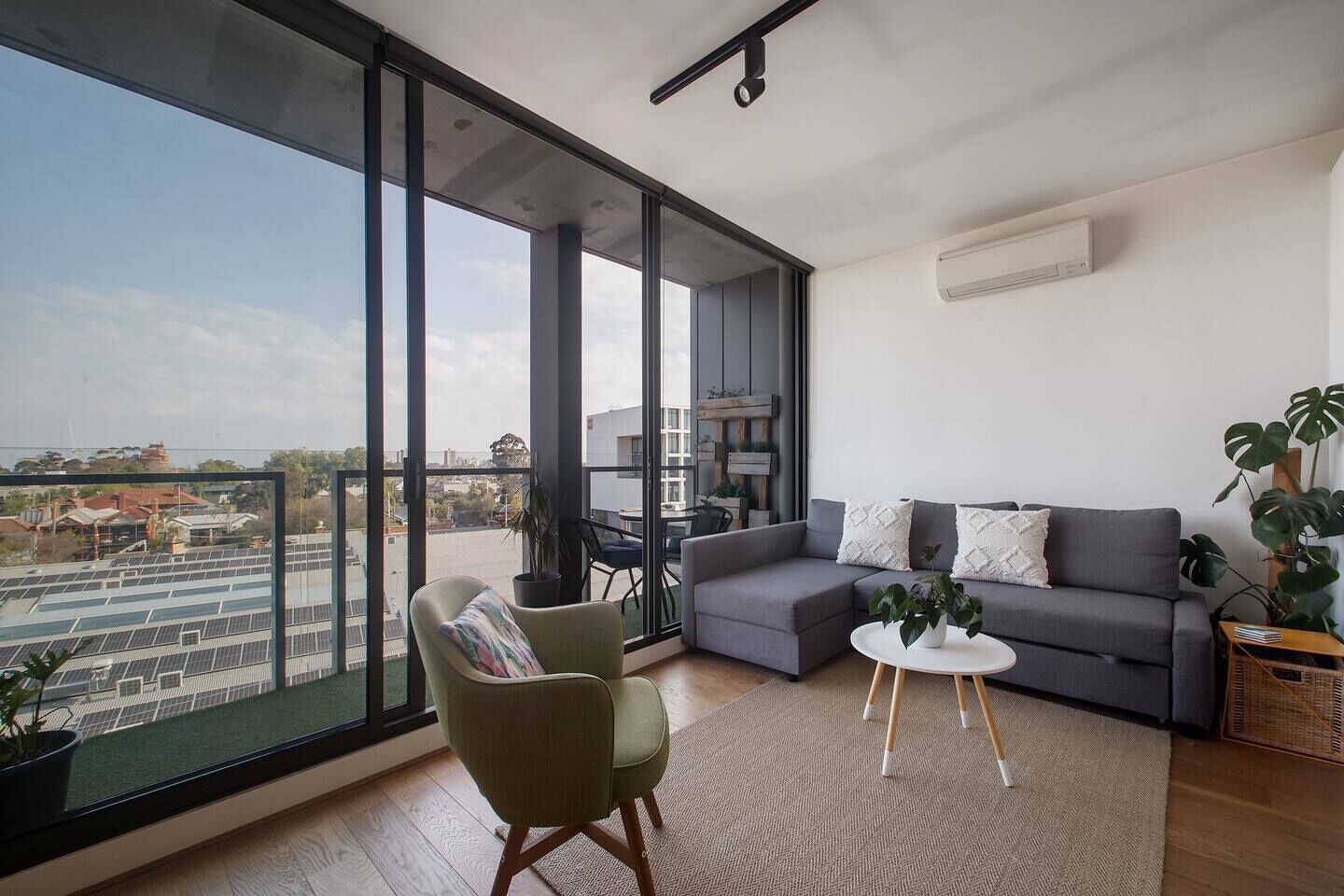 A modern living room with a large window, a grey sofa, a small round table, and a green armchair.