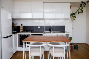 A modern kitchen with white cabinets, a wooden table, two white chairs, a stove, and a sink. - Eden of Abbotsford A Serene Escape off Johnston St (Abbotsford)