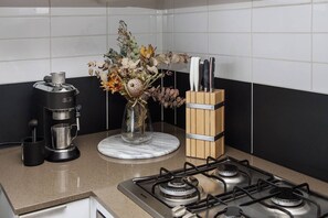 Une cuisine équipée d’une machine à café, d’un vase contenant des fleurs séchées et d’un bloc à couteaux posé sur le plan de travail.