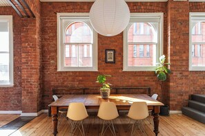 A dining area with a wooden table, four chairs, a hanging plant, and large windows with arched tops. - Foy and Gibson An Industrial Chic Historic Warehouse (Collingwood)