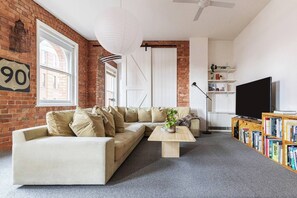Een woonkamer met een bakstenen muur, een bank, een bijzettafeltje, een boekenkast en een televisietoestel.