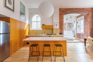 A modern kitchen with a large island, wooden cabinets, and a brick accent wall. - Foy and Gibson An Industrial Chic Historic Warehouse (Collingwood)