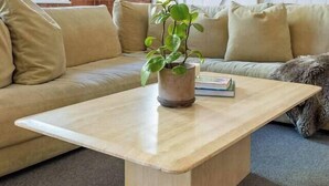 Una habitación con pared de ladrillo, puerta corredera blanca, sofá color beige y mesa de centro de madera con una planta.