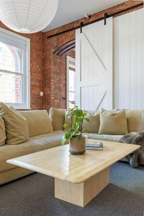 A room with a brick wall, a white sliding door, a beige sofa, and a wooden coffee table with a plant. - Foy and Gibson An Industrial Chic Historic Warehouse (Collingwood)