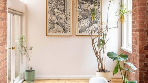 Un salón de conferencias con una mesa de madera, sillas blancas, dos cuadros con vistas urbanas y plantas en macetas.