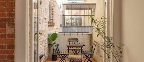 A wooden deck with a table and chairs, a potted plant, and a view of a brick building.