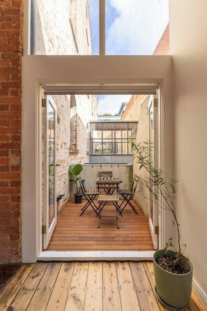 A wooden deck with a table and chairs, a potted plant, and a view of a brick building. - Foy and Gibson An Industrial Chic Historic Warehouse (Collingwood)