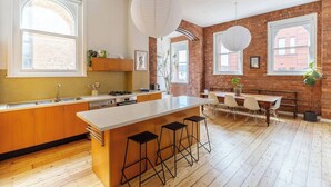 Una cocina moderna con una isla grande, armarios de madera y un comedor con pared de ladrillo de fondo.